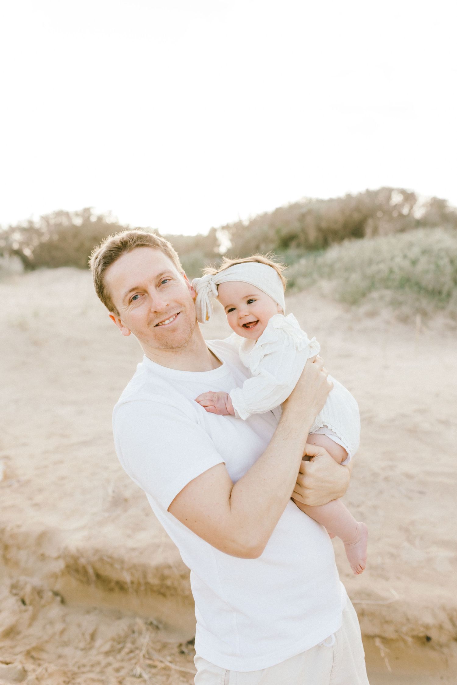 A series of joyful moments captured at the beach with a parent and baby in white outfits playing in the sand.