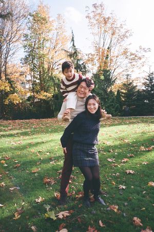 Two people play together on an autumn lawn with fallen leaves and evergreen trees in the background.