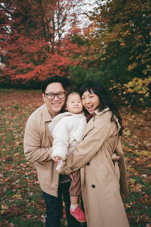A family wearing matching beige coats shares joyful moments together among vibrant red autumn foliage.