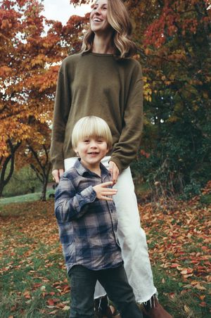 A child in a plaid shirt plays with cotton candy against a backdrop of autumn trees with orange leaves.