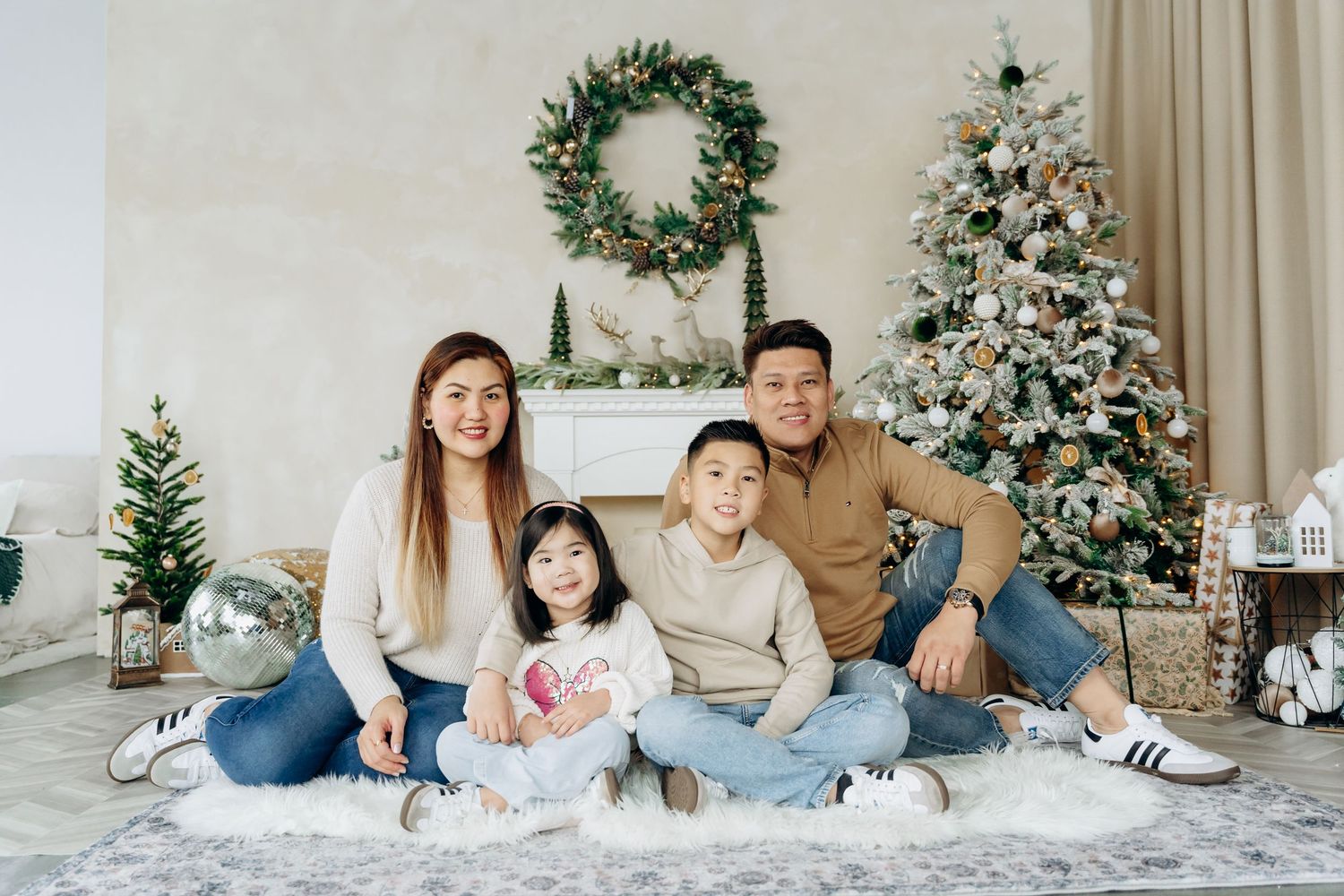 A family in coordinating white and beige outfits poses together in front of a decorated Christmas tree for holiday photos.