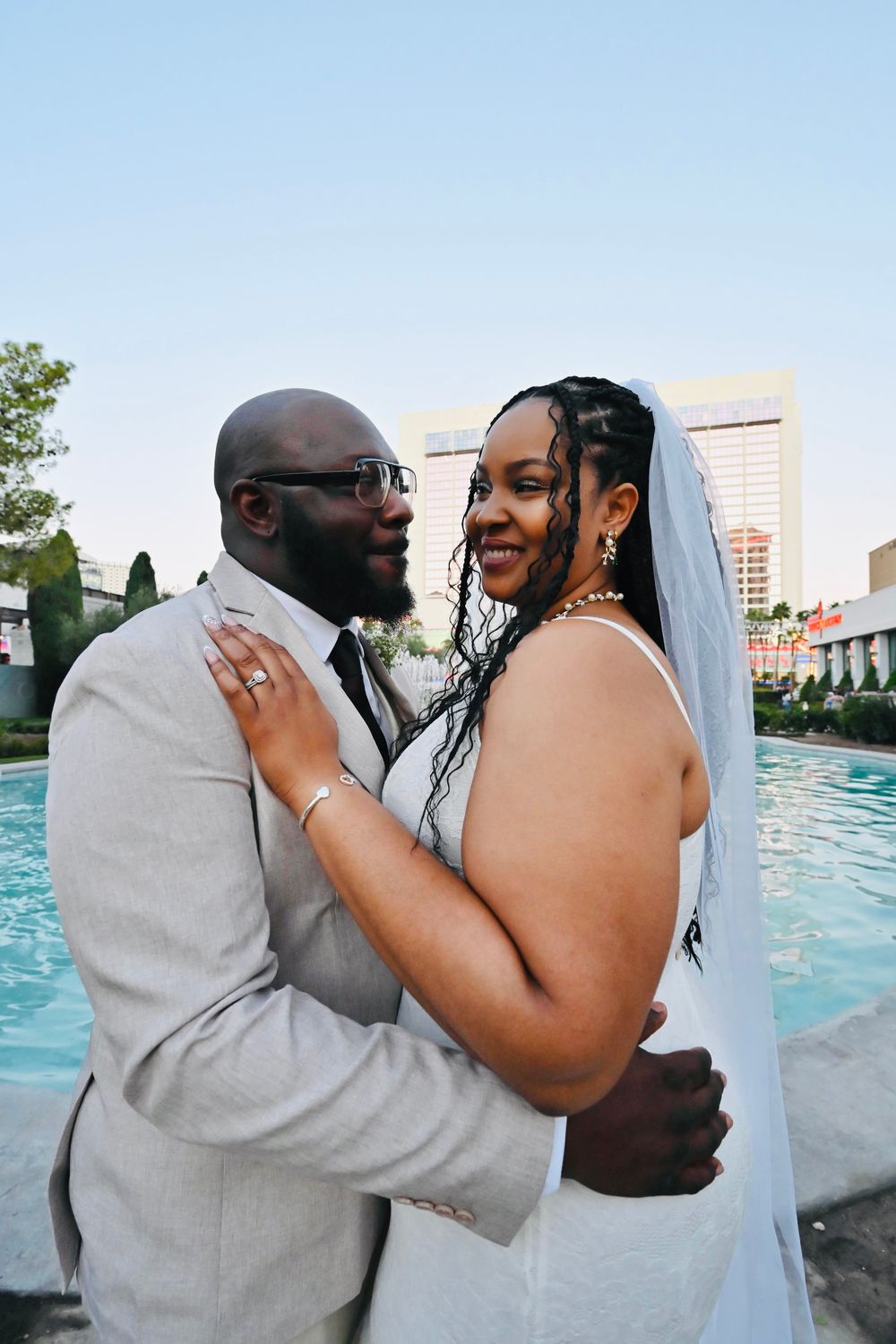 Joyful bride laughs as groom holds her close near a Las Vegas pool during their wedding photo session.