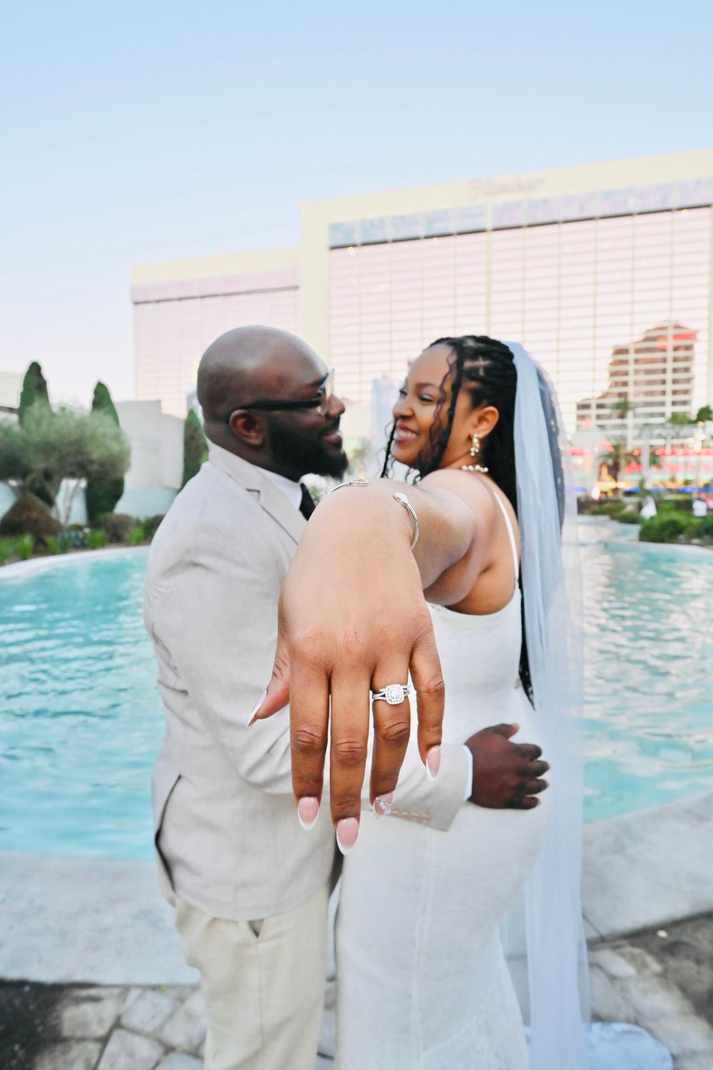 Newlyweds display their wedding ring while embracing poolside at a Las Vegas resort on their wedding day.