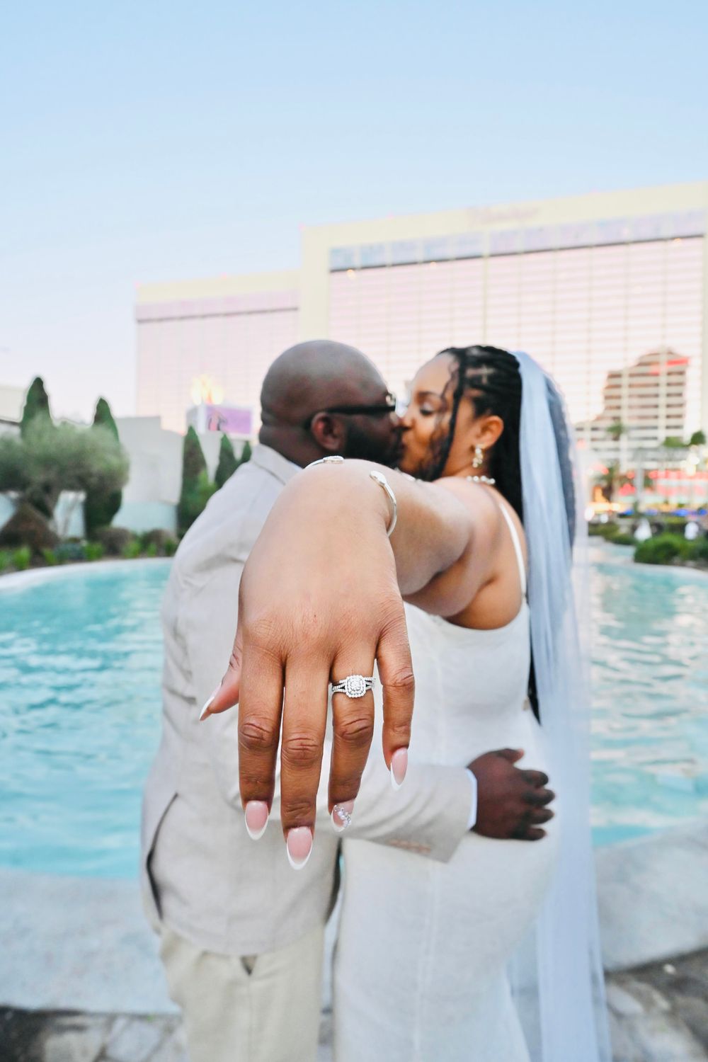 Bride shows off her diamond wedding ring while kissing groom poolside at a Las Vegas resort.