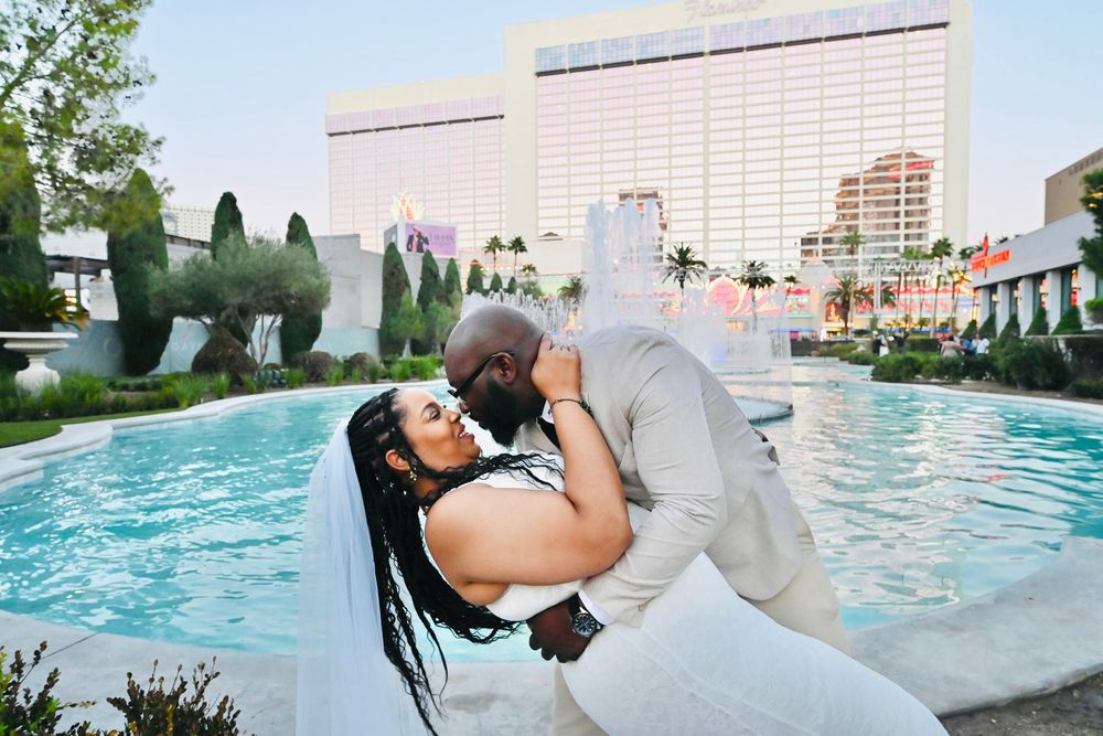 Groom dips bride for a romantic kiss in front of a Las Vegas resort fountain on their wedding day.