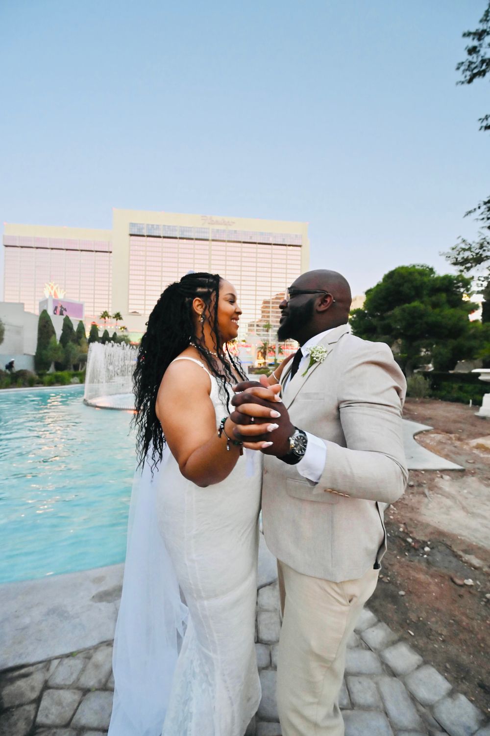 Newlyweds dancing and holding drinks together by a resort pool in Las Vegas on their wedding day.