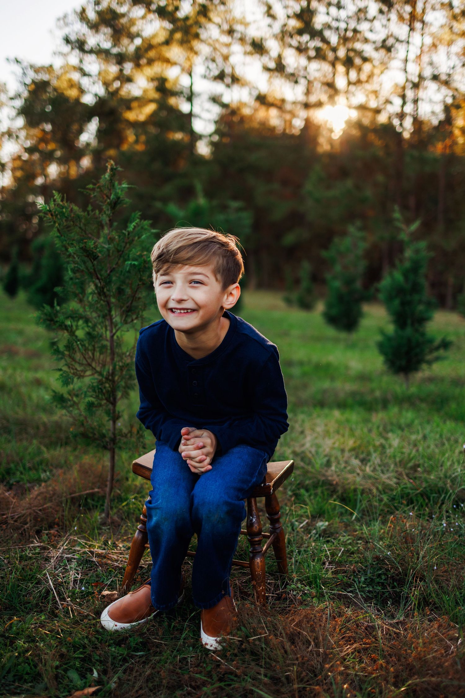 A child sits in a wooden chair outdoors at sunset among evergreen trees, showing joyful expressions in a photo series.