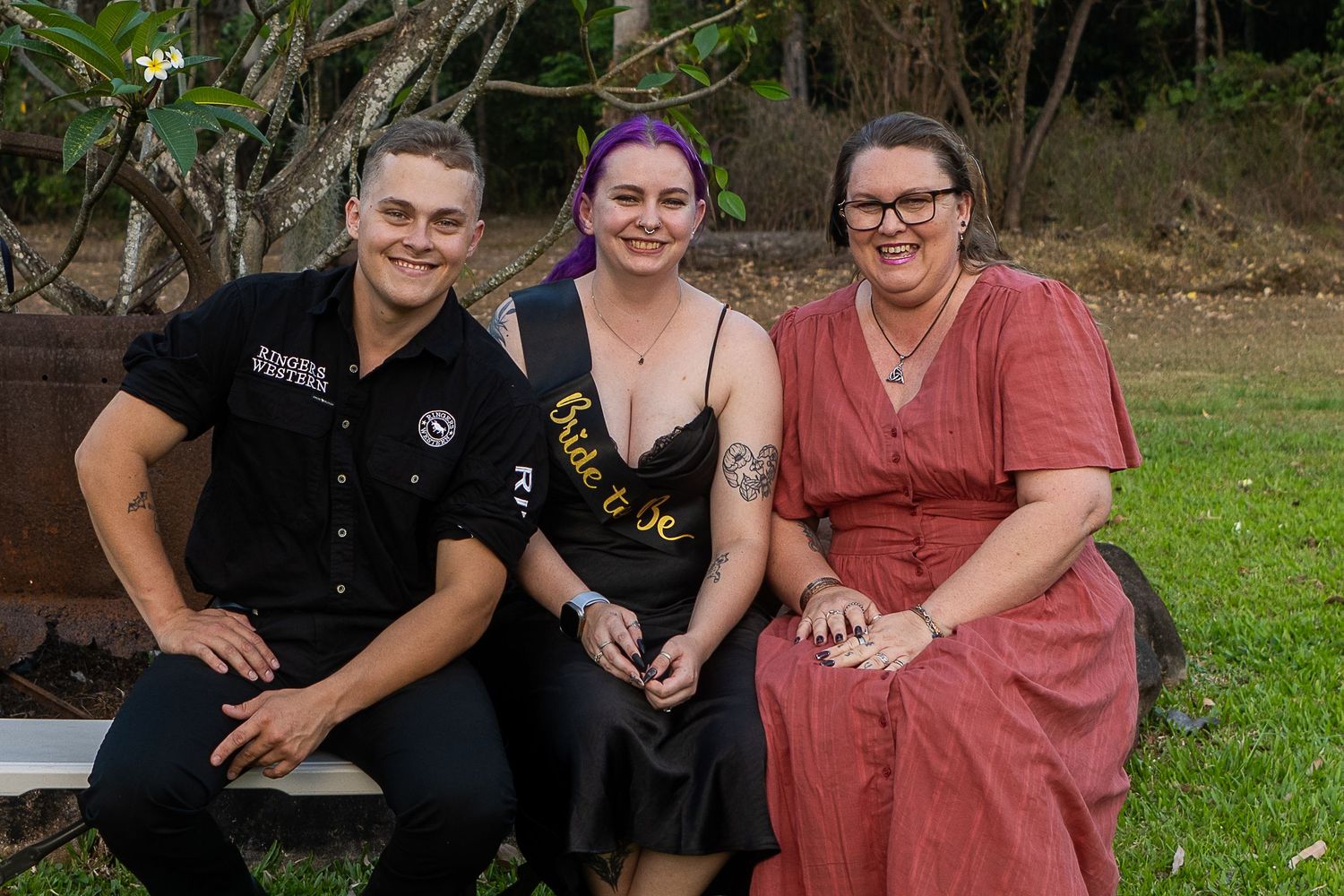 Three people sit together outdoors smiling at the camera.