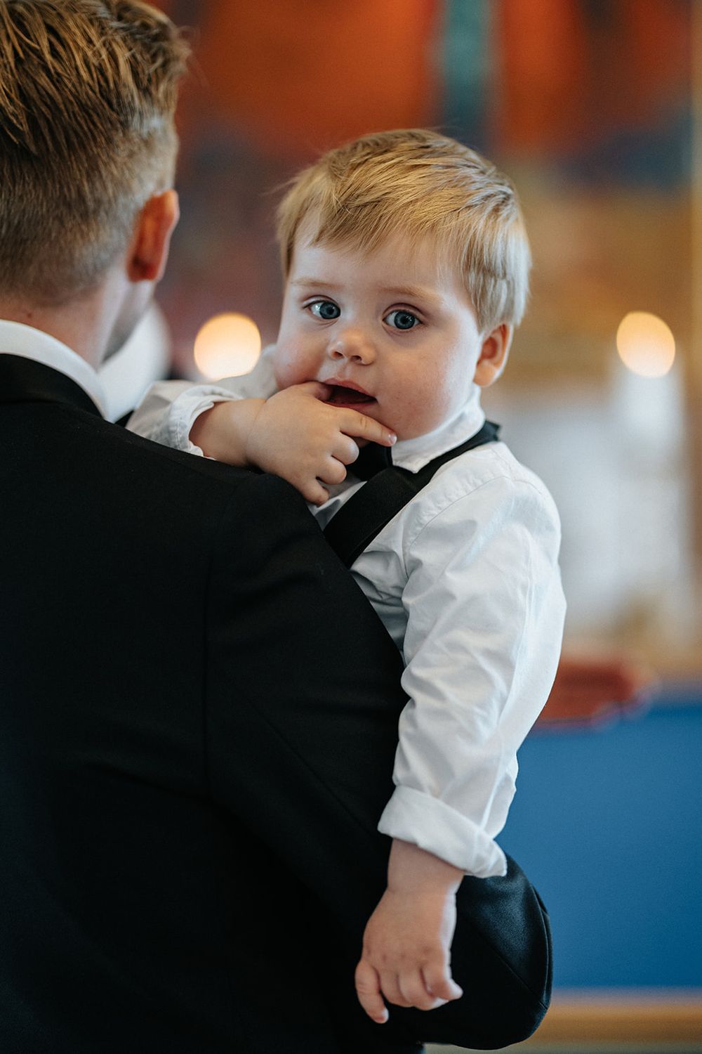 A small child in a white shirt being held and comforted by someone wearing a black suit during a formal event.