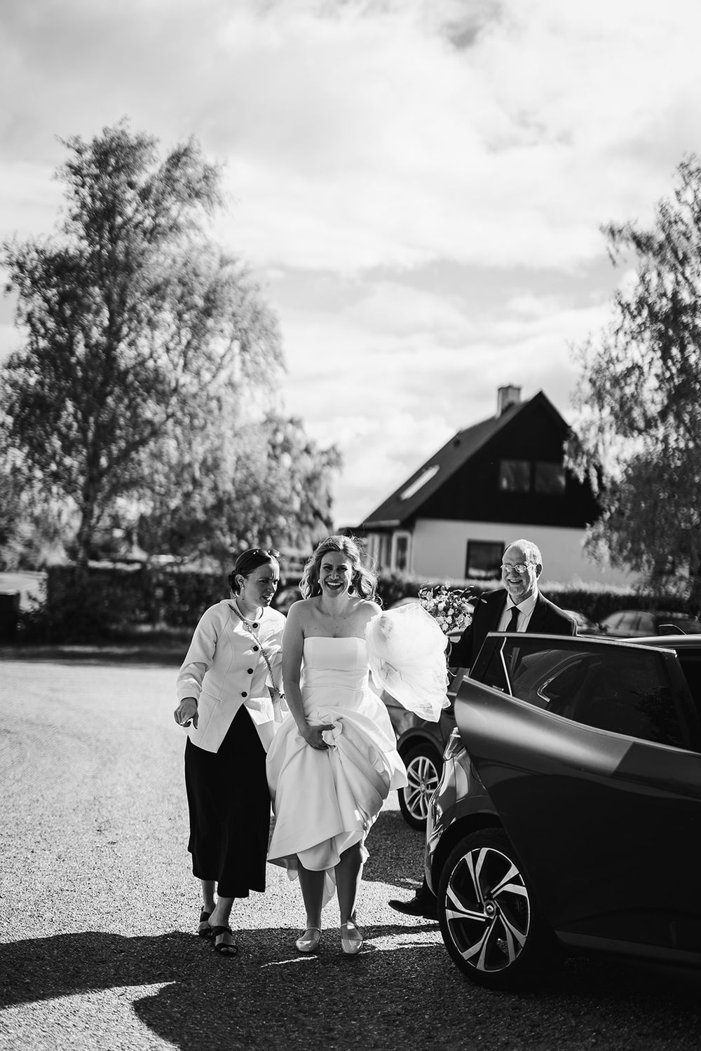 Two small children in white outfits walking together near a vintage car on a sunny day.