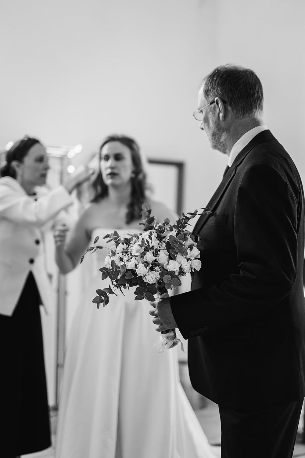 Black and white photo of a wedding preparation moment with a beautiful bouquet of white flowers held by a suited figure.