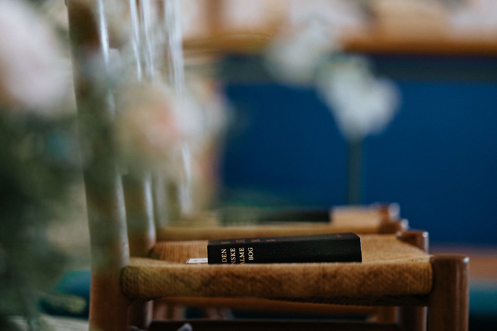 A leather-bound Bible rests on a wooden church pew with soft bokeh lighting in the background.