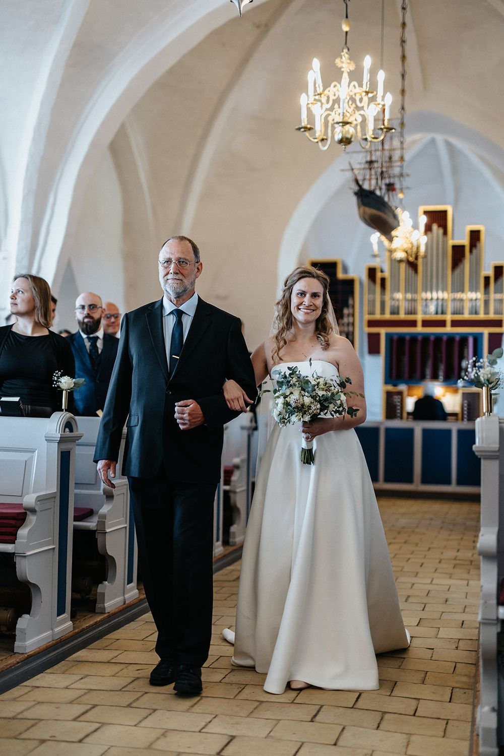 Wedding couple shares a joyful dance moment on elegant stone floor under crystal chandeliers.