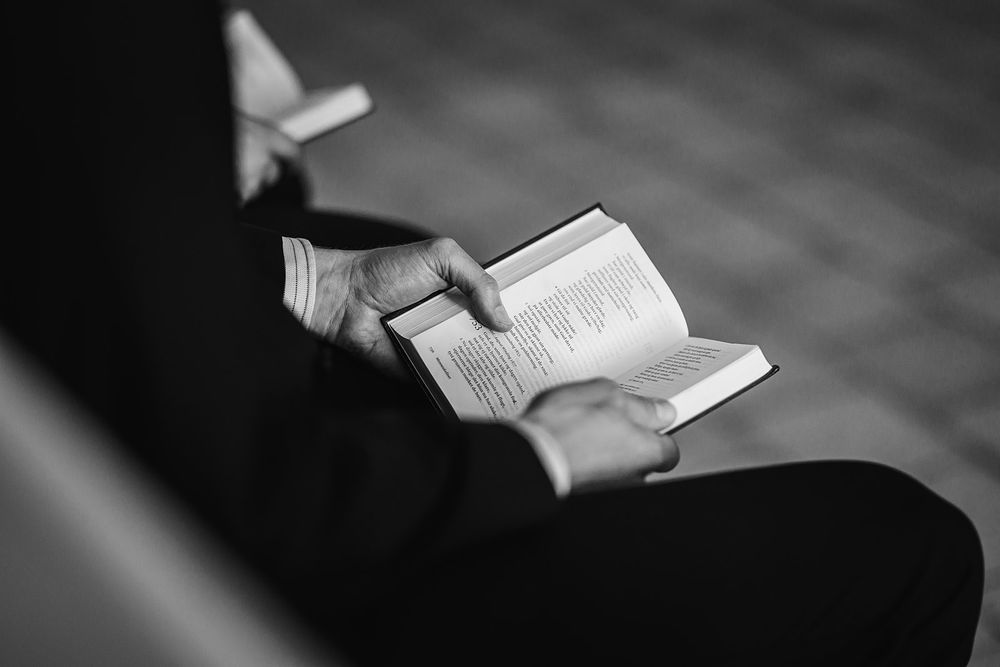 Black and white close-up of hands holding open books during a wedding ceremony.