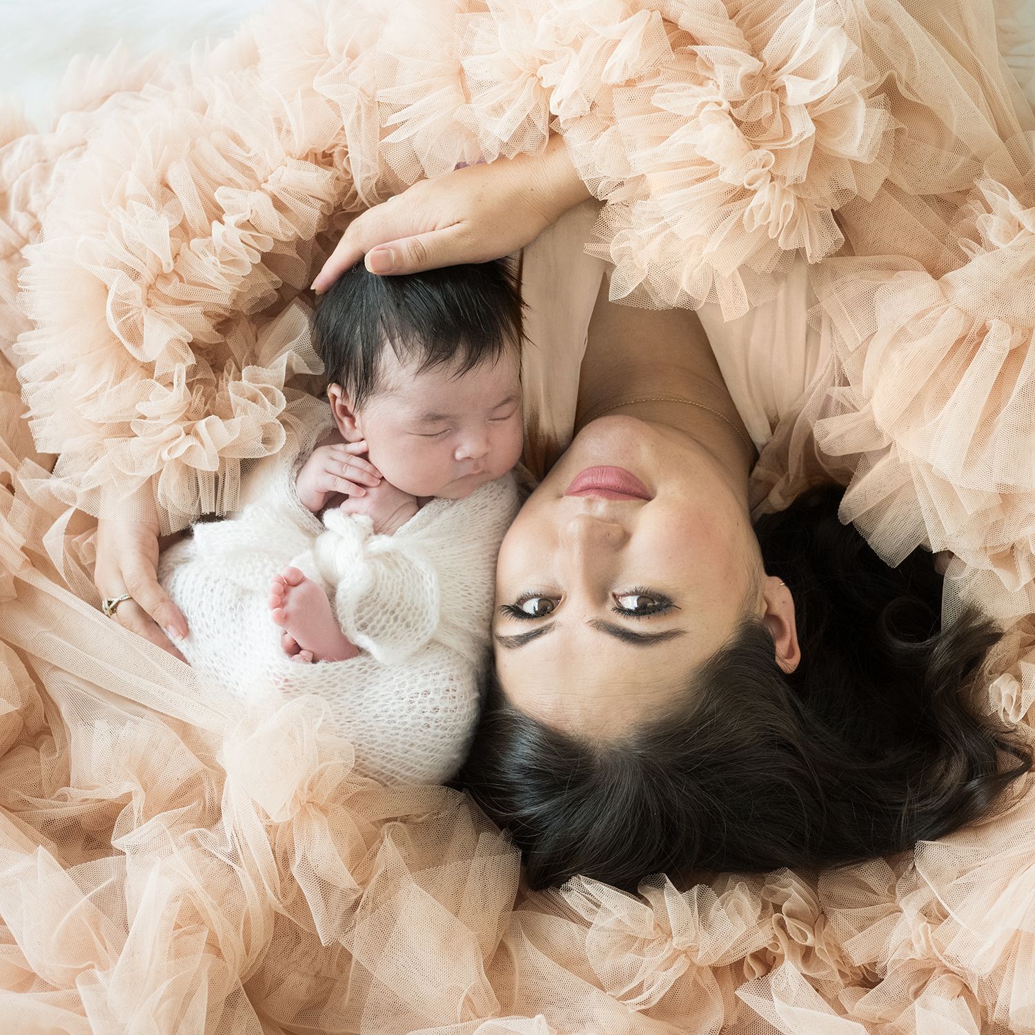 Dreamy newborn portrait with baby and parent on peach tulle fabric background.