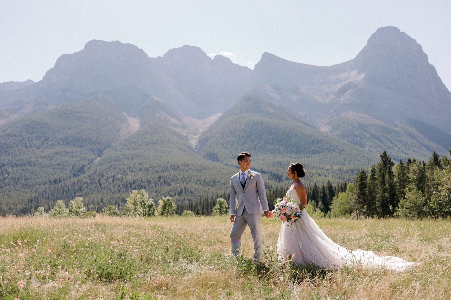 A couple poses in a scenic mountain meadow with dramatic peaks and green landscape in the background.