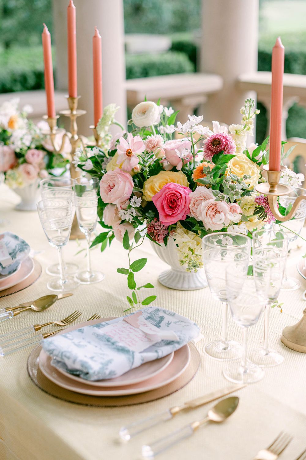 Elegant table setting with pink roses, coral candles, and blue napkins arranged on white plates for a romantic dinner.