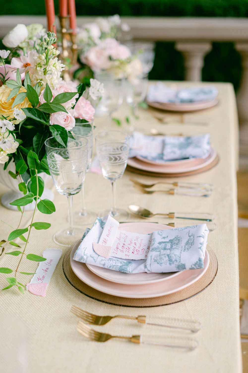 Elegant table setting with pink floral centerpieces, gold charger plates, and delicate blue napkins.