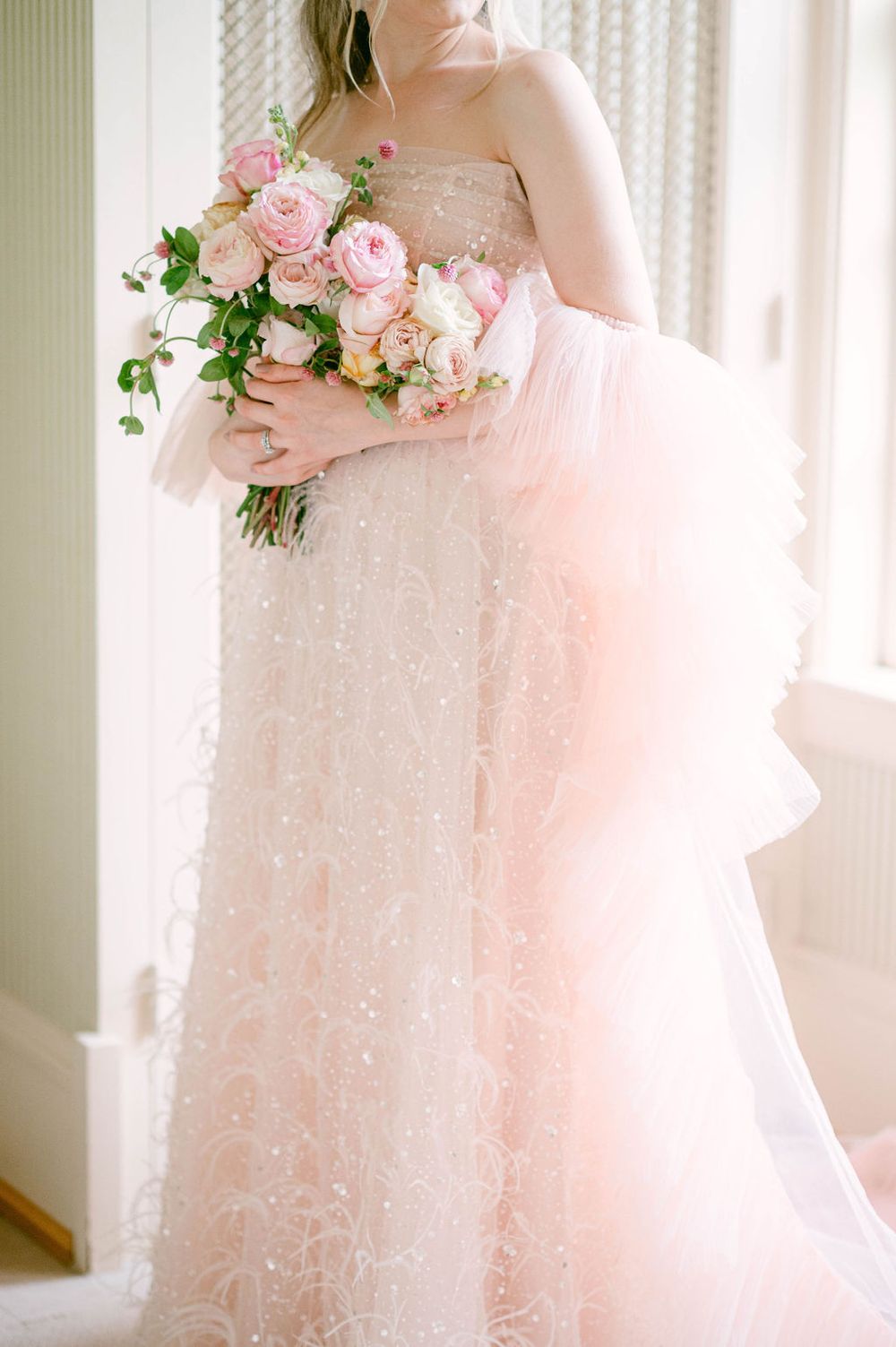 Blush pink wedding gown with delicate floral details and soft tulle layers captured in natural light.