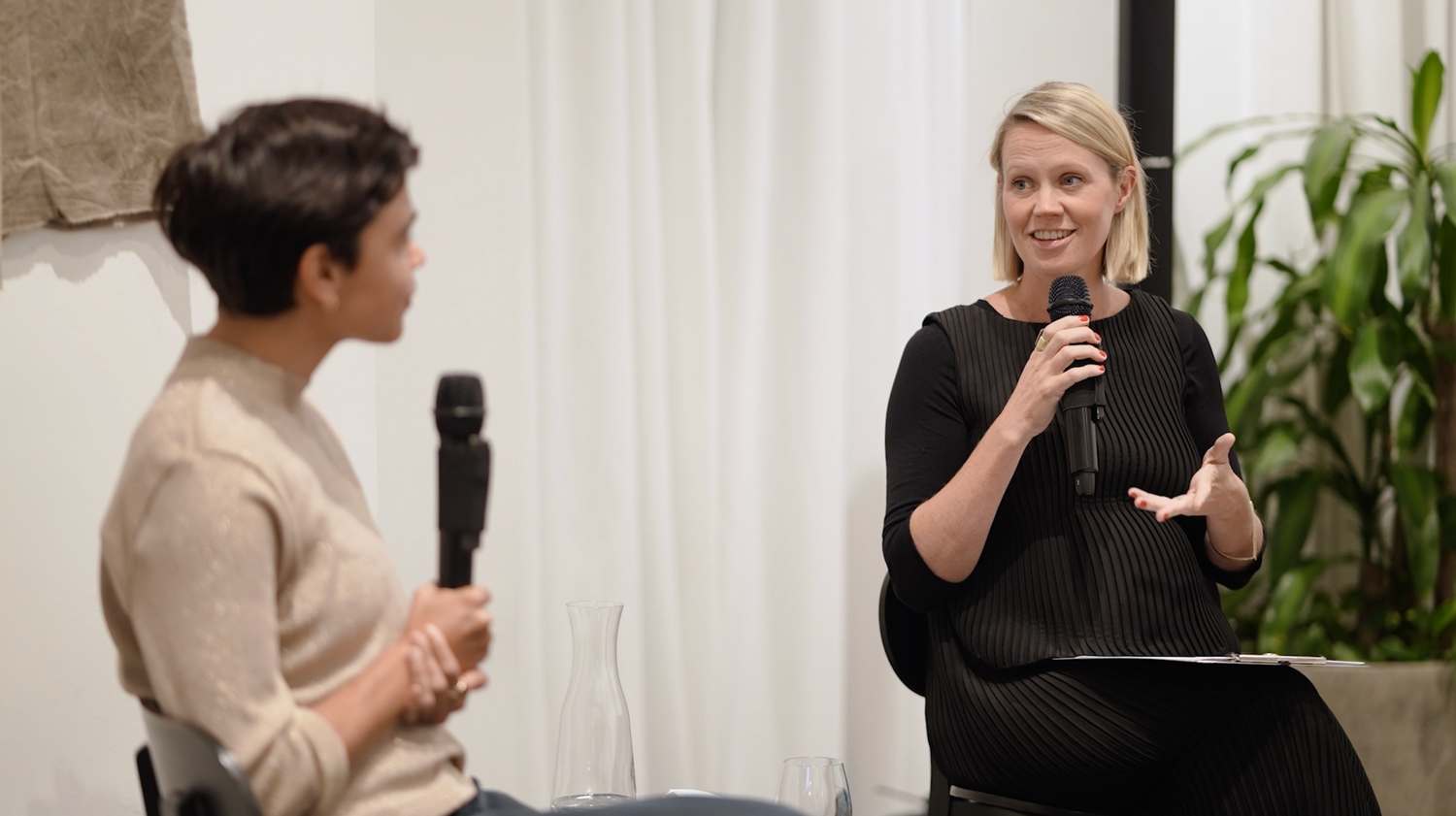 Two speakers engage in conversation during a professional event with microphones.