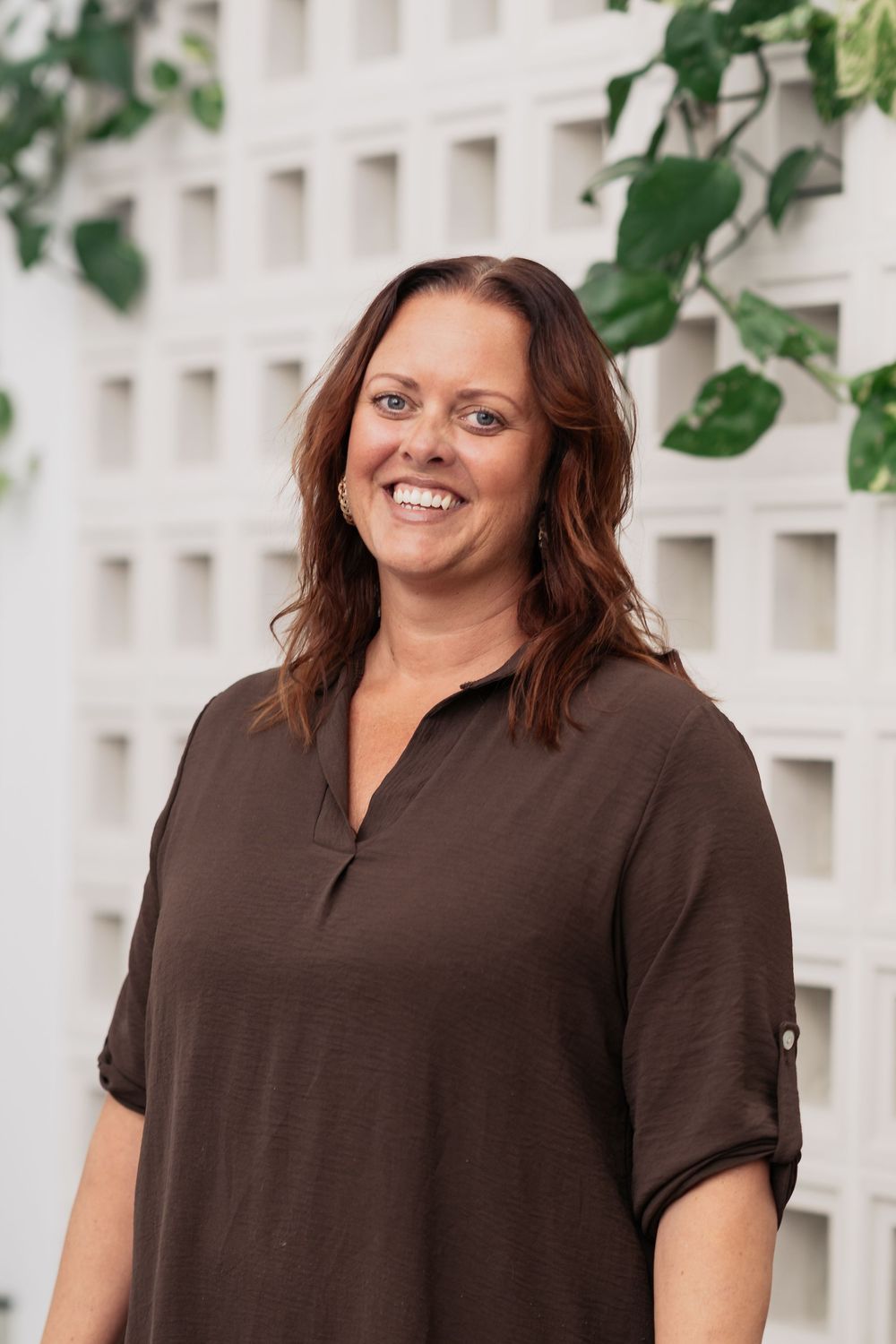 Professional headshots of person in brown shirt against white architectural background with greenery.