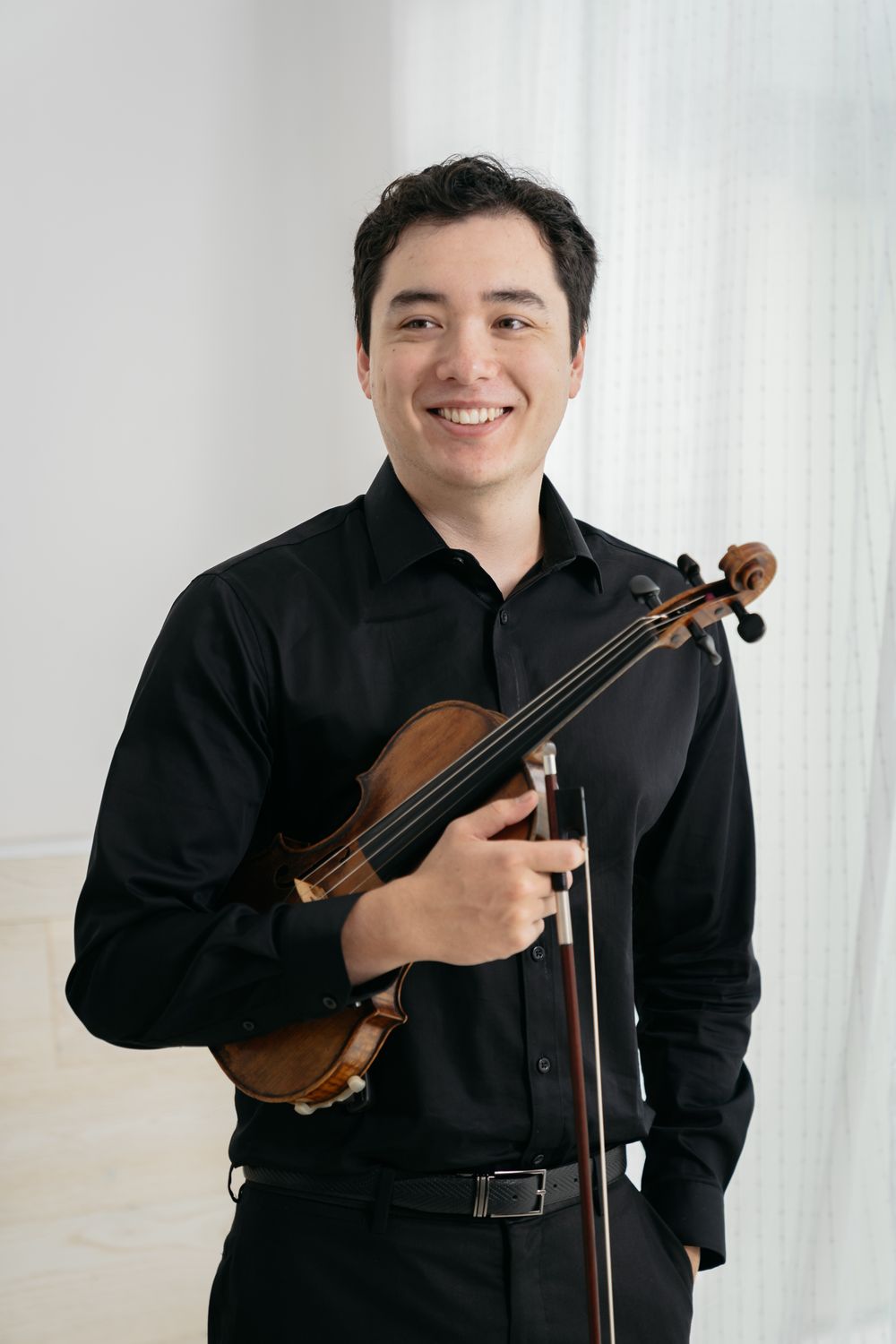 Professional musician poses with violin in formal black attire against white background.