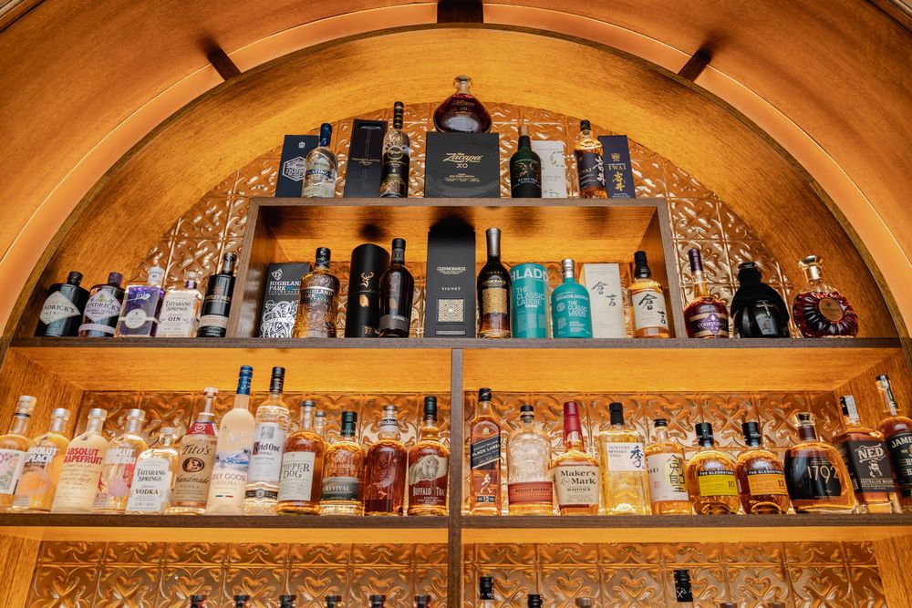 Extensive collection of liquor bottles displayed on curved wooden shelving with warm lighting.