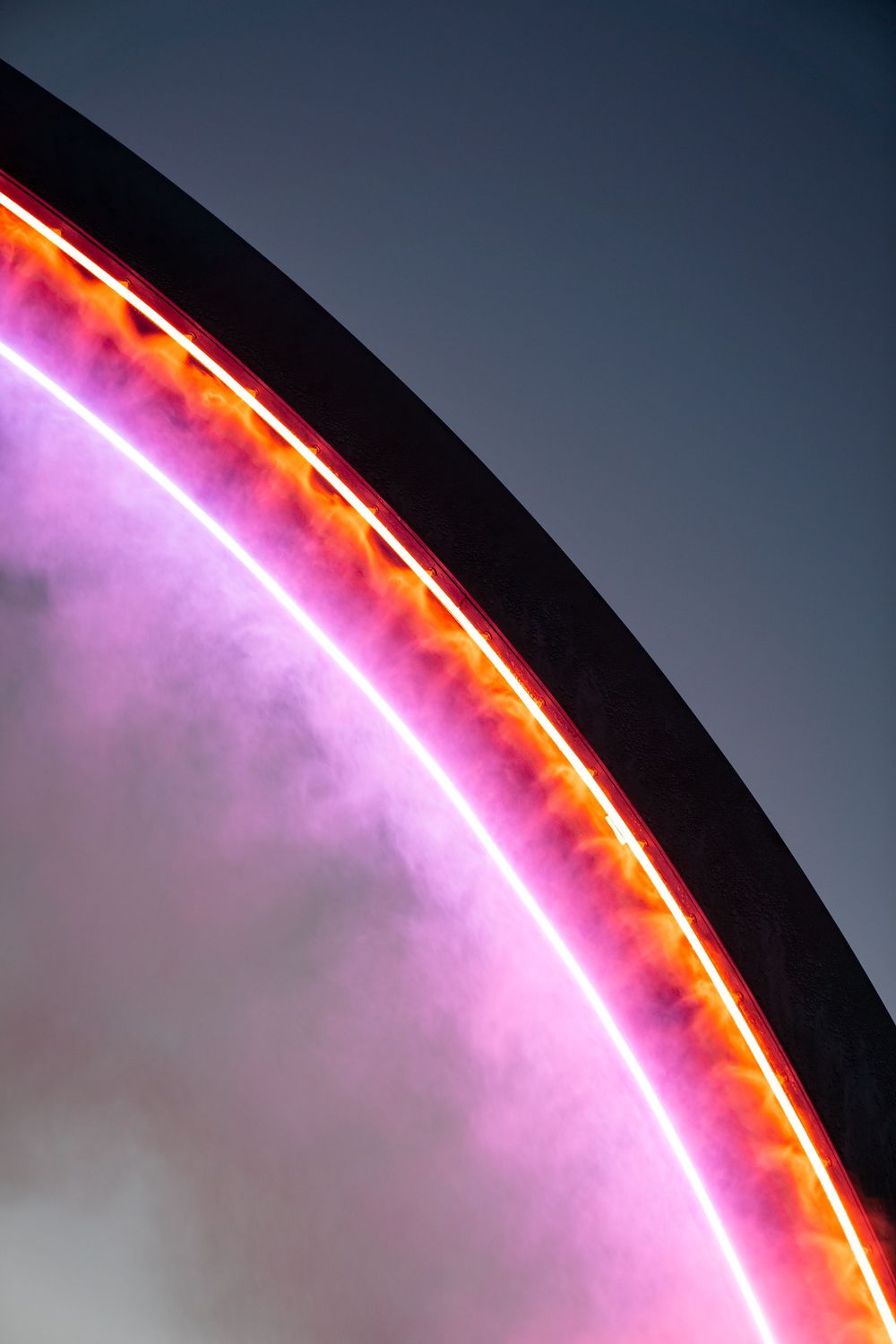 Close-up of curved neon lights in pink and orange against dark sky.