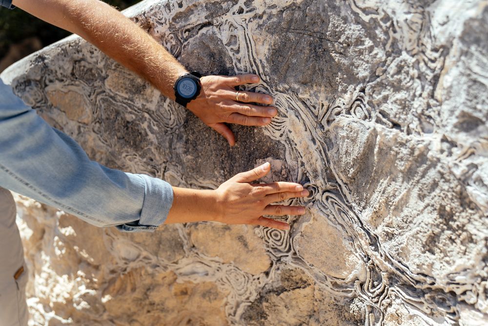 Close-up shots of hands touching textured rock or stone surfaces.