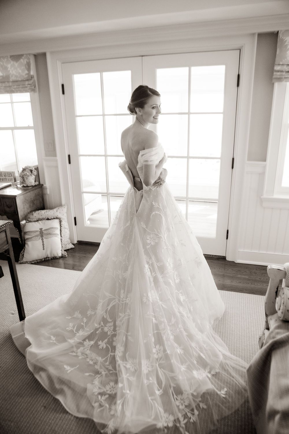 Elegant bride in lace wedding gown posing by French doors in black and white.