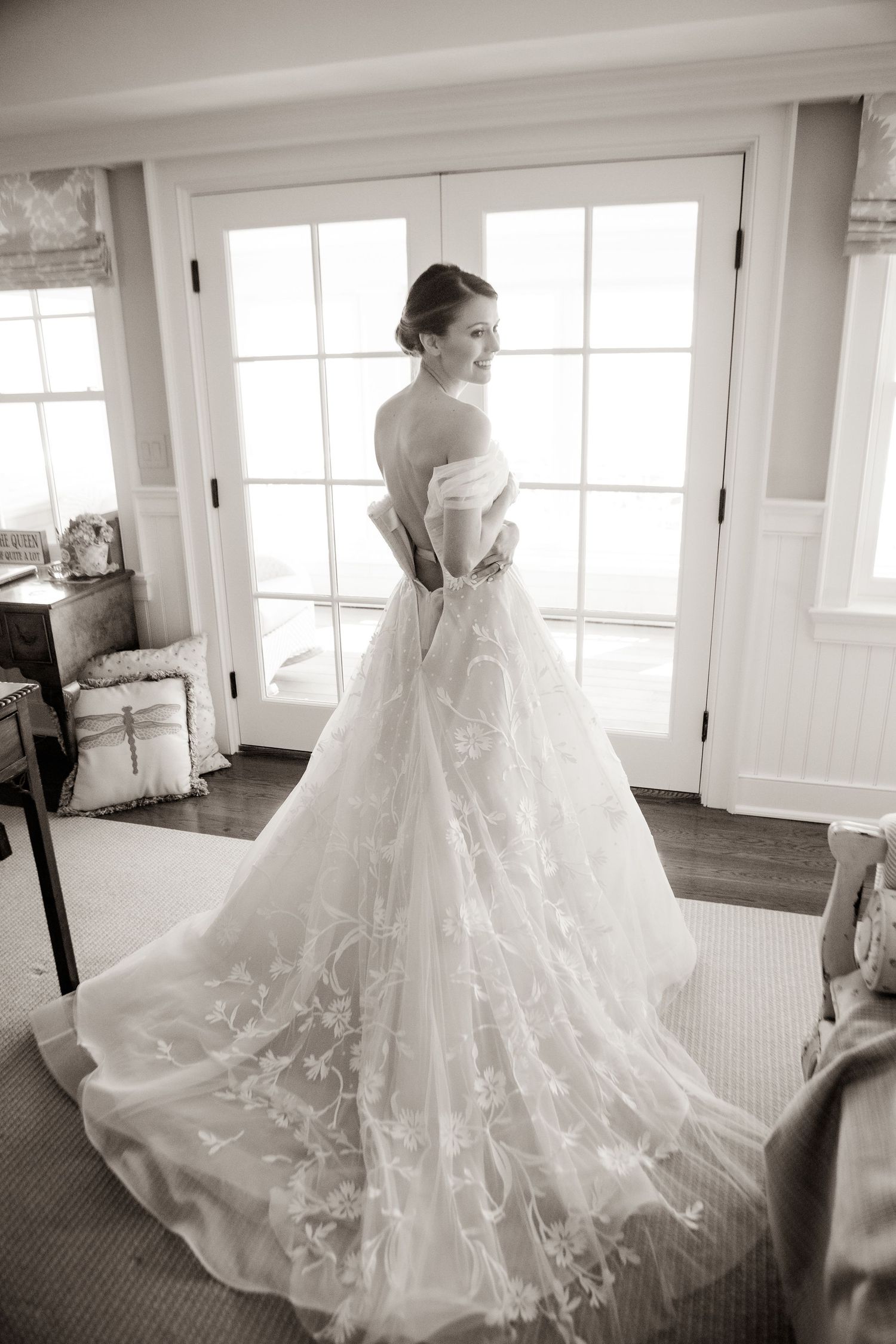 Elegant bride in lace wedding gown posing by French doors in black and white.
