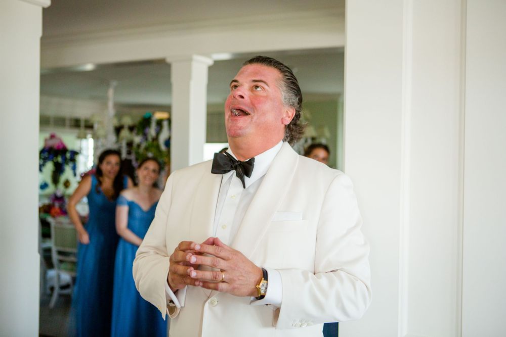 A man in a white tuxedo jacket shows emotion during a wedding ceremony.