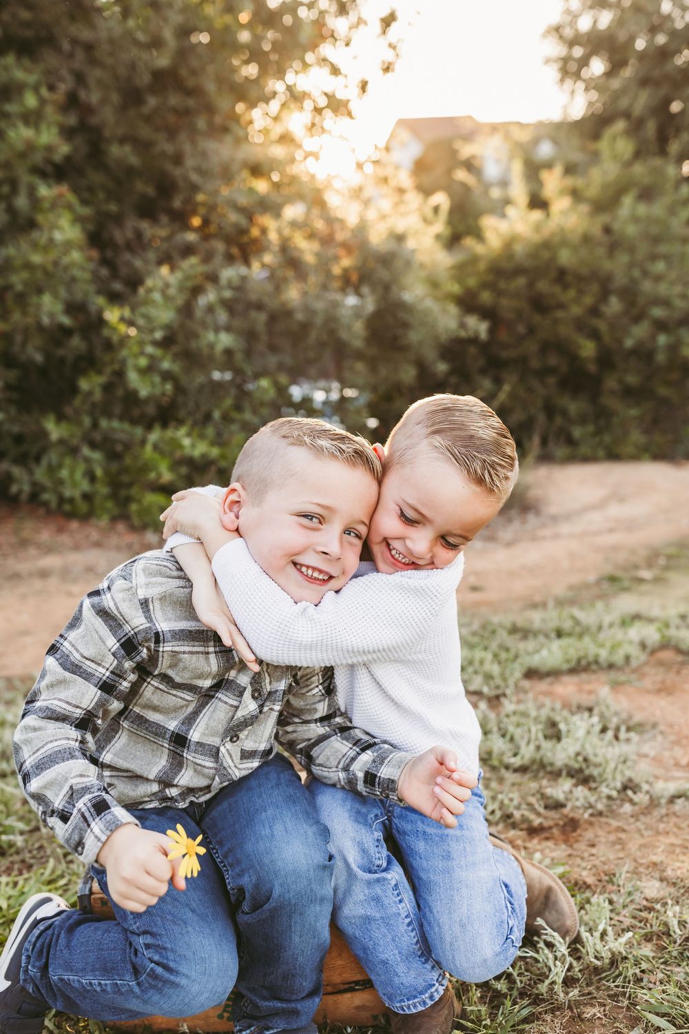 Two children in plaid shirts and jeans share playful moments together at sunset in a grassy outdoor setting.