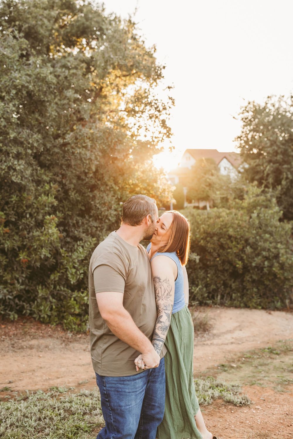 A couple shares a romantic moment at sunset in a rustic outdoor setting surrounded by trees and golden light.
