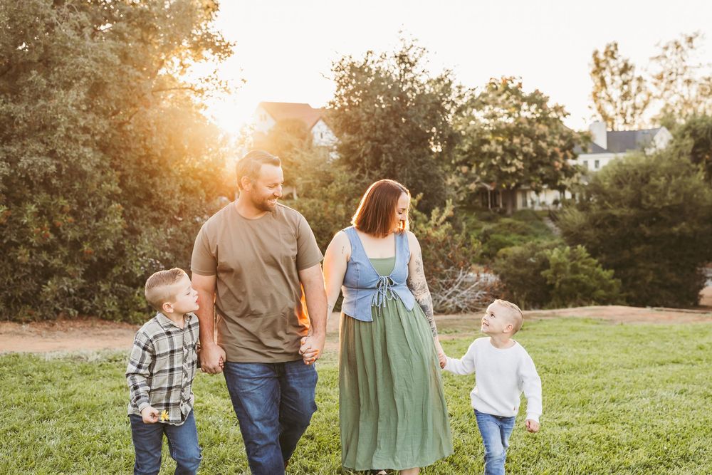 A family walks together through a sunlit meadow at golden hour during a warm summer evening.