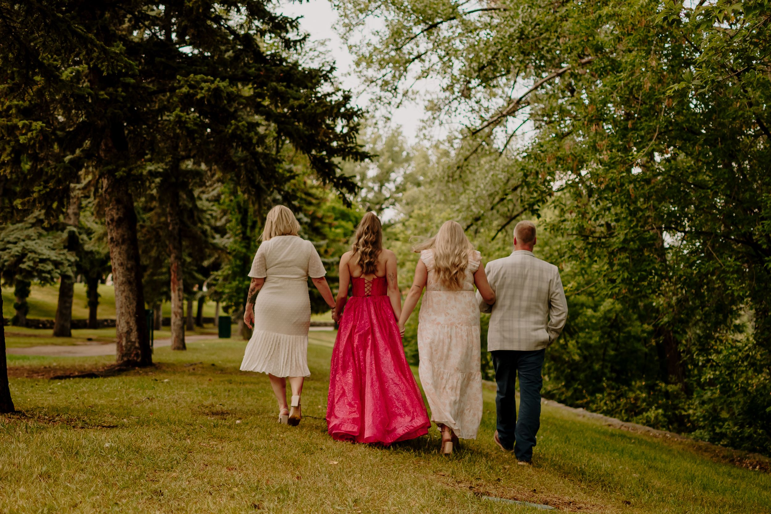 Wedding party walks together through a lush green park on a sunny afternoon.