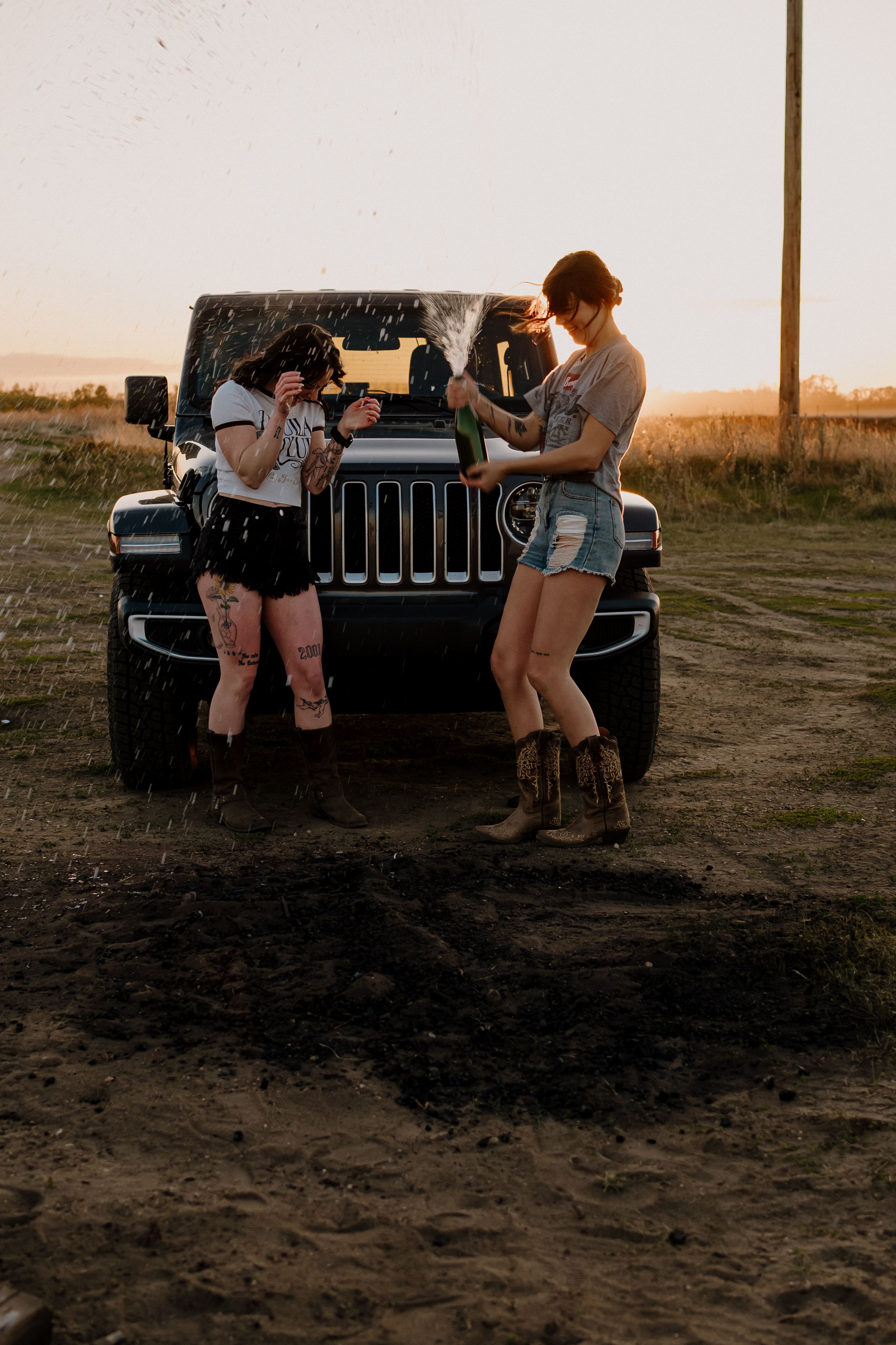 Two people hanging out by a black Jeep during sunset on dirt ground.