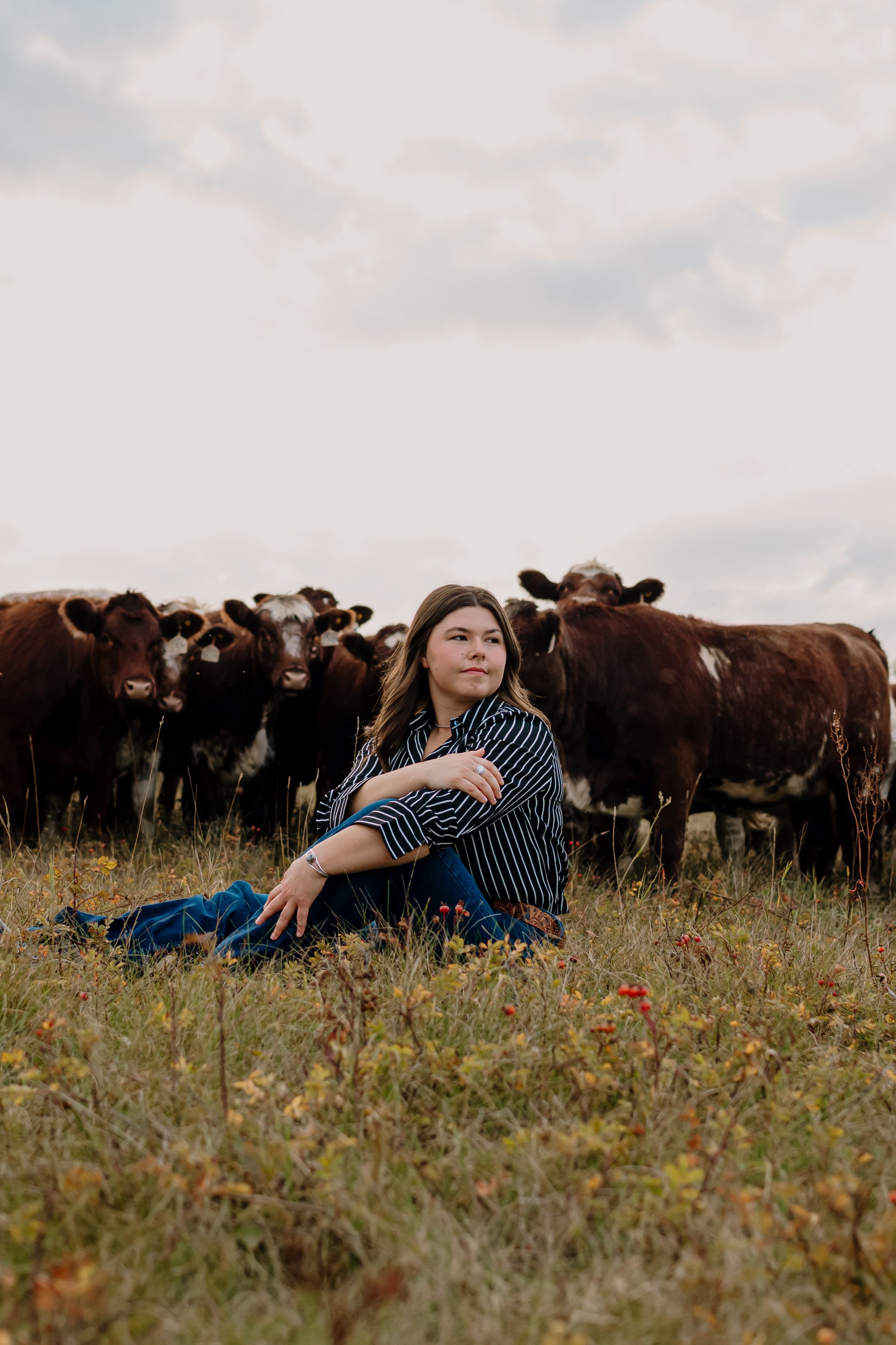 A relaxed pose in a wildflower field with a herd of cattle visible in the background.