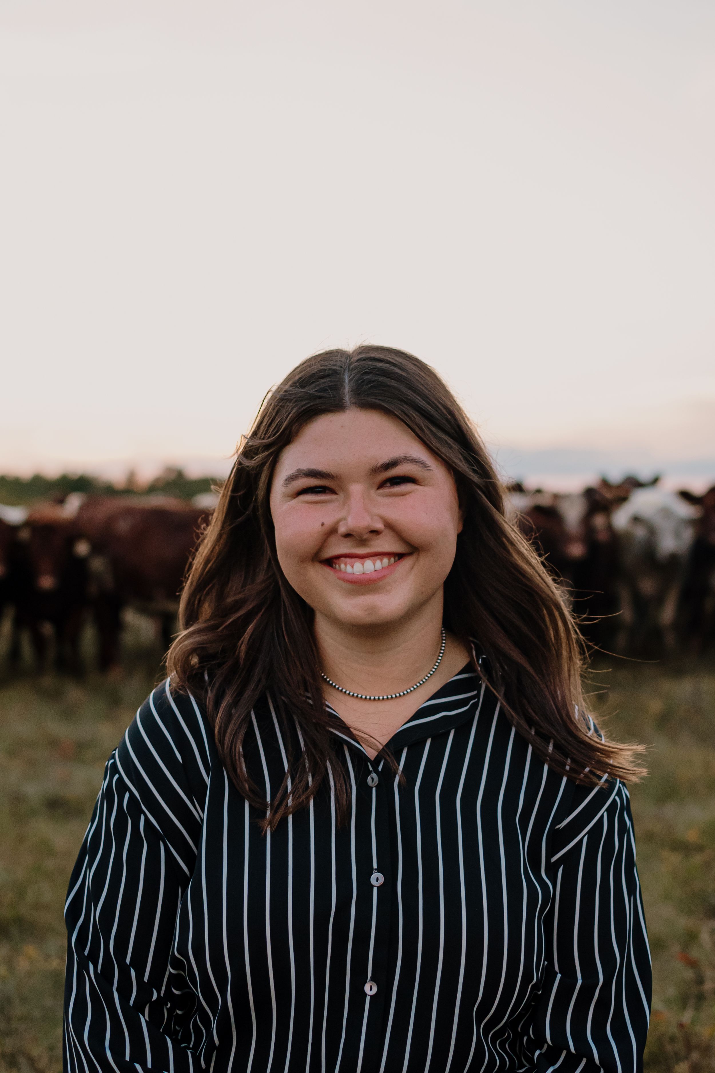 A joyful portrait in a striped shirt with windswept hair against a field with cattle in the background.