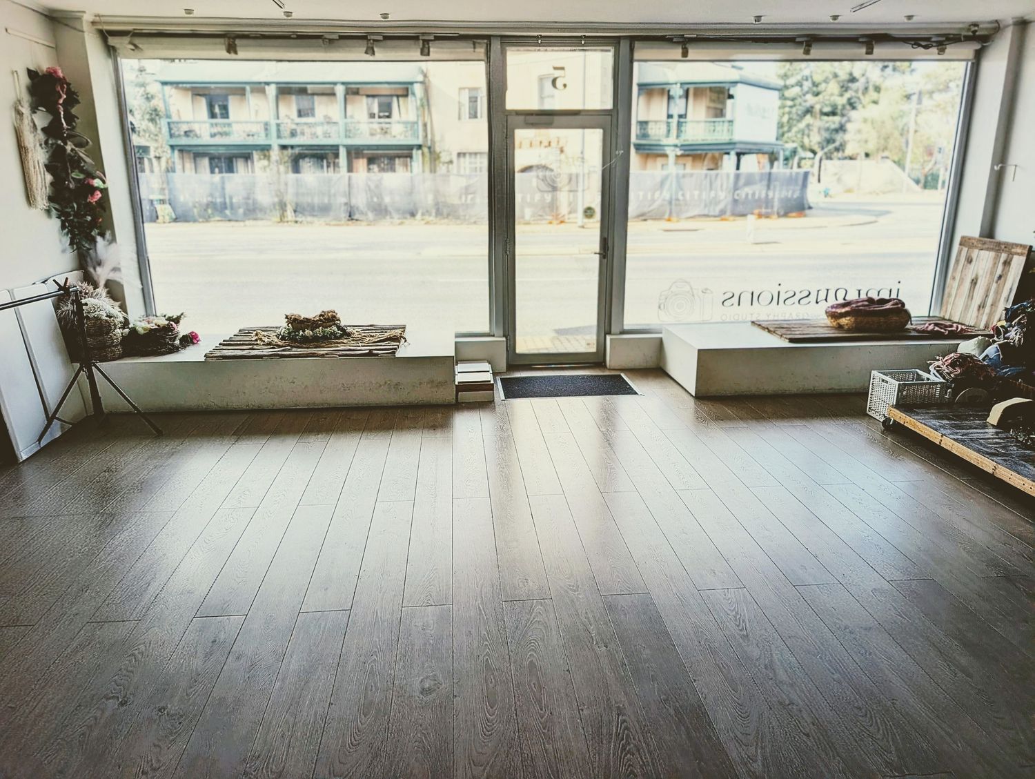 Spacious retail or yoga studio interior with hardwood floors, large storefront windows, and natural light overlooking a parking lot.