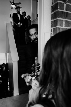 Black and white candid wedding photo of groom on staircase with guests in foreground.