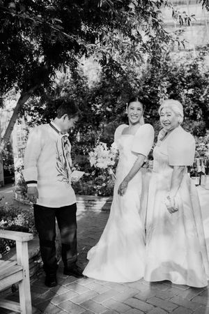 Bride in white gown smiling with family members outdoors in a black and white garden wedding photo.