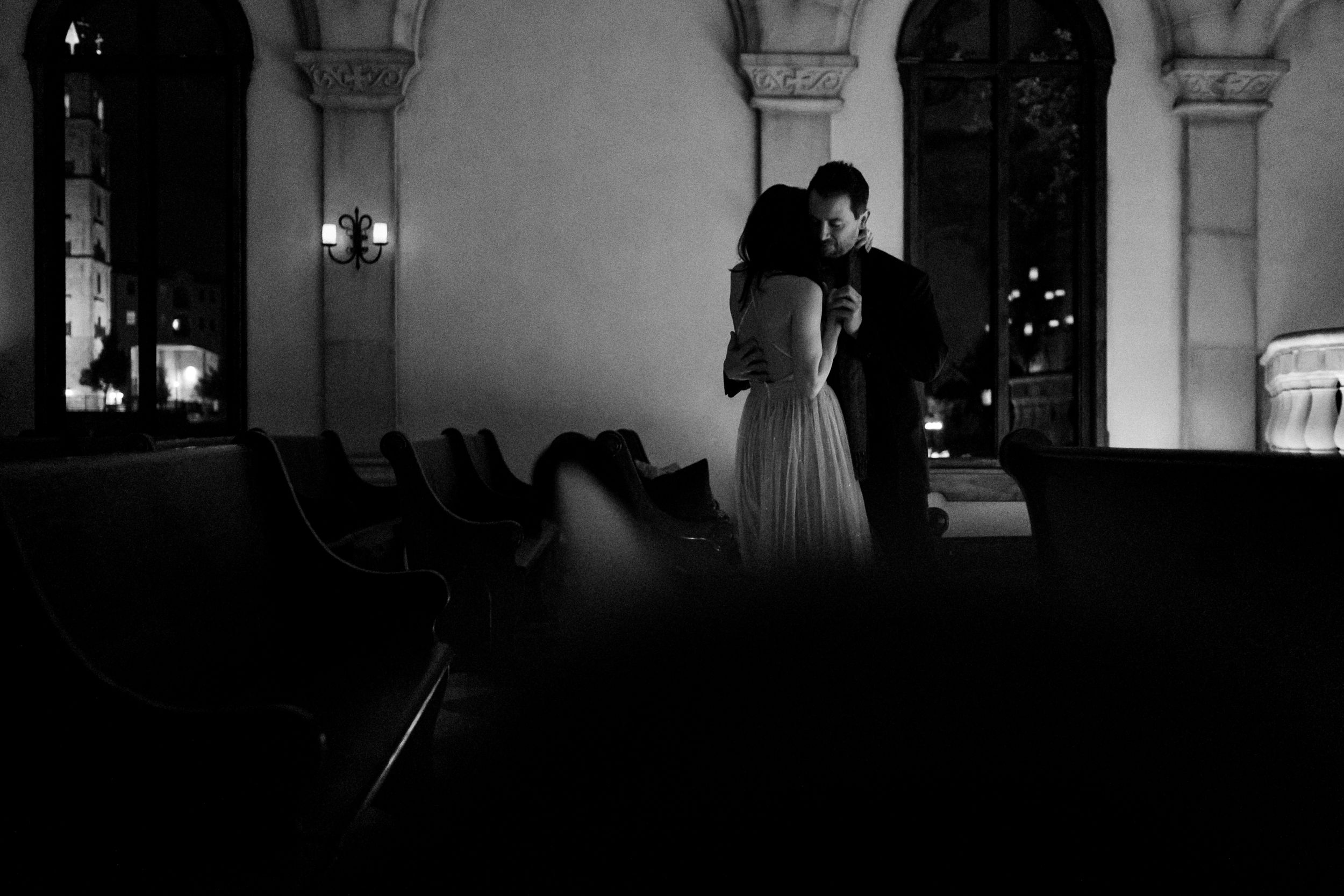 Black and white romantic silhouette of bride and groom embracing in ornate church.