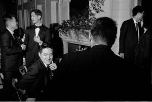 Black and white candid photo of wedding guests in formal attire socializing at reception.