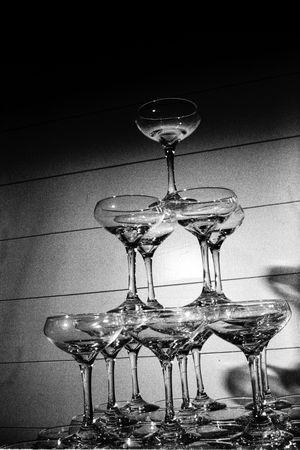 Elegant pyramid tower of champagne coupe glasses photographed in dramatic black and white lighting.