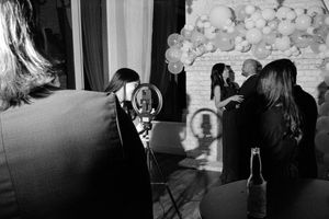 Behind-the-scenes black and white photo of wedding guests being photographed at a balloon backdrop reception.