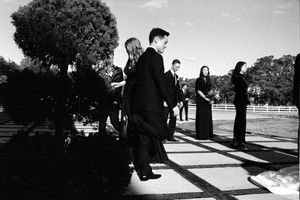 Wedding party dressed in black walking along a sunlit pathway in a black and white outdoor photograph.