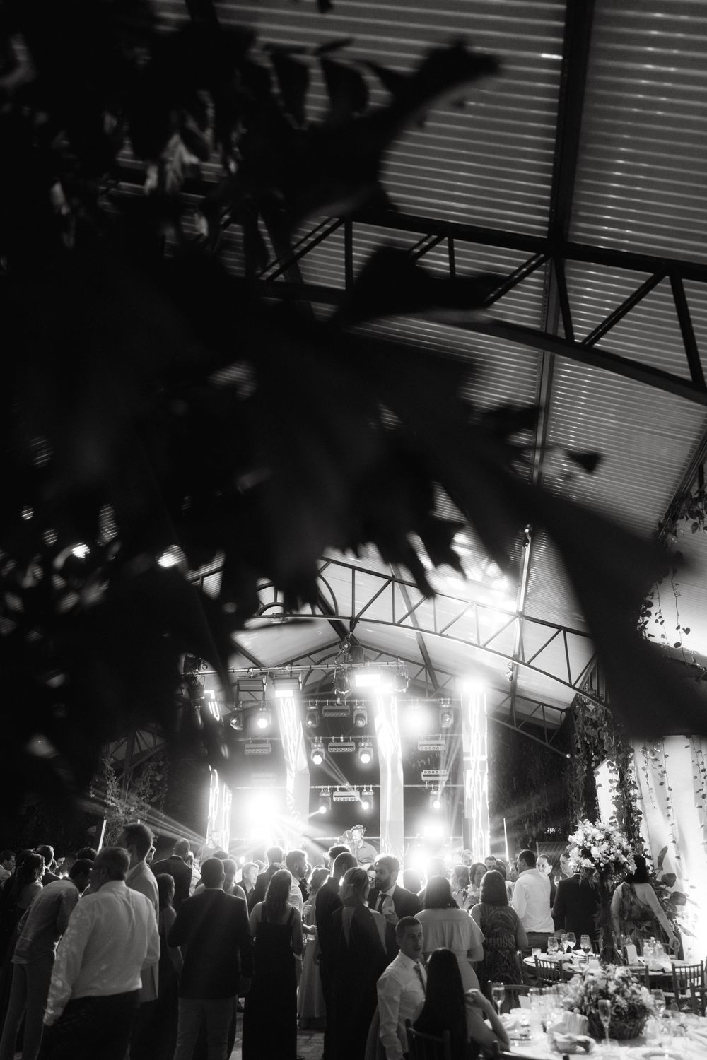A dimly lit wedding reception venue with bright stage lights illuminating a crowded dance floor during an evening celebration.