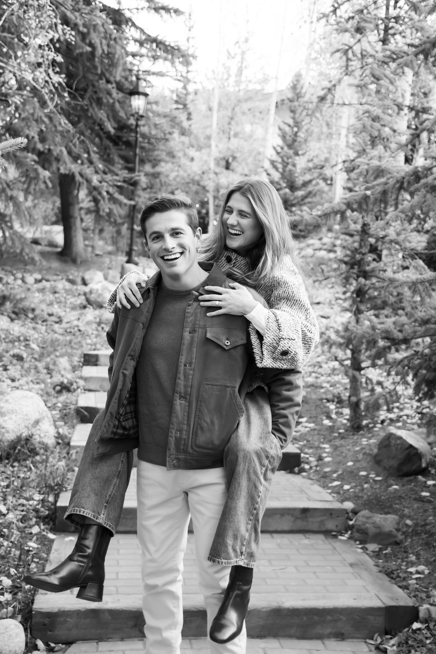 An artsy black and white photo of a laughing couple piggy back taken in Vail Village Colorado after a surprise proposal