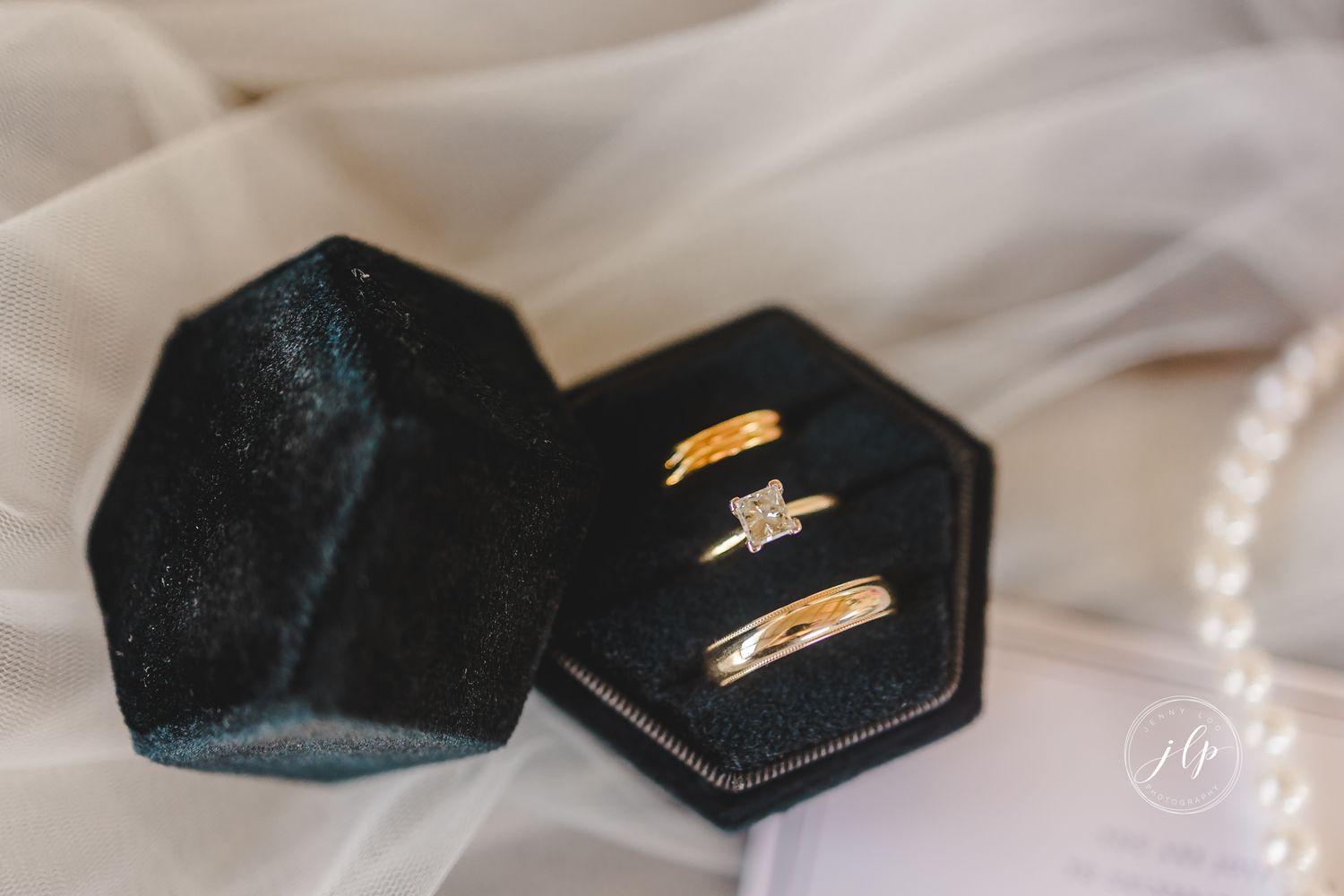 Wedding rings displayed in black hexagonal boxes on white fabric with soft lighting.